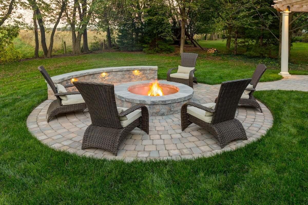 A well-crafted fire pit surrounded by chairs, set in a beautifully landscaped yard. The circular patio made of pavers complements the fire pit, creating an inviting outdoor living space.