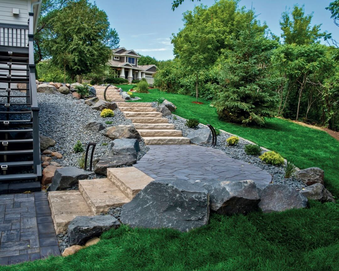A beautifully designed landscape with a stone pathway and steps leading up to a fully landscaped area