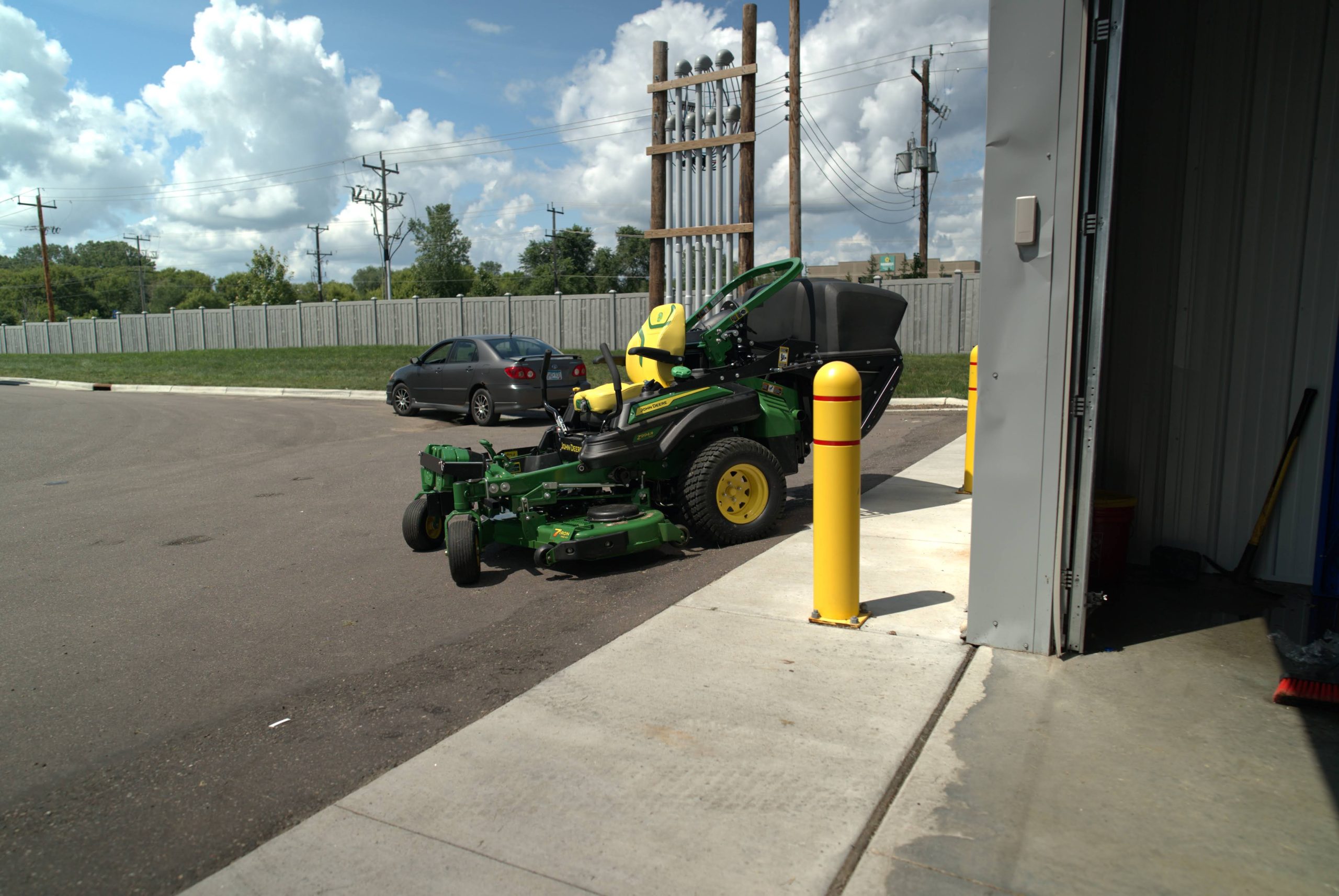 A commercial lawn mower parked near a service building beside a grassy area.