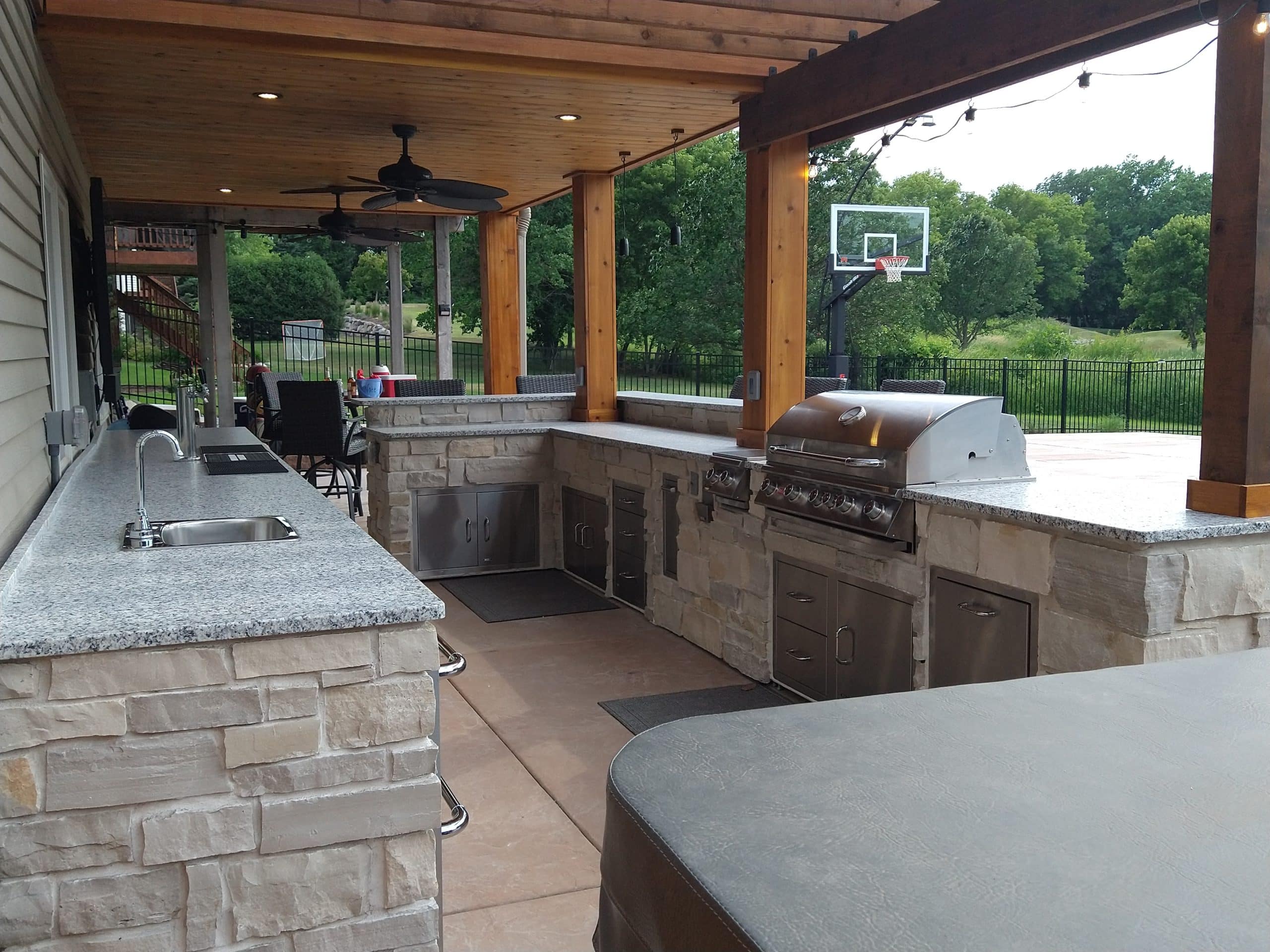 A custom stone outdoor kitchen with granite countertops and a built-in grill under a wooden cover.