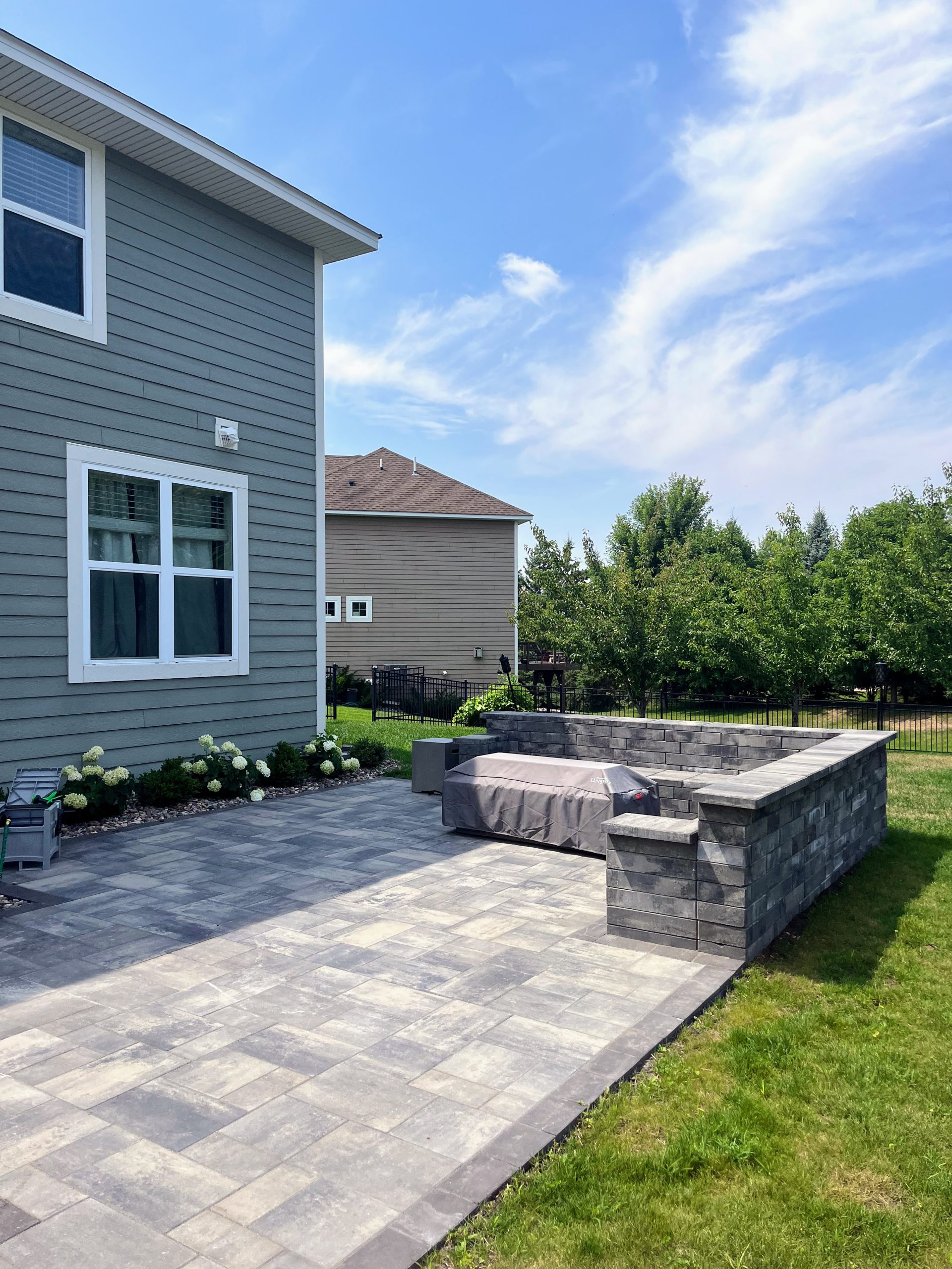 A newly installed paver patio with a stone seating wall in a backyard setting.