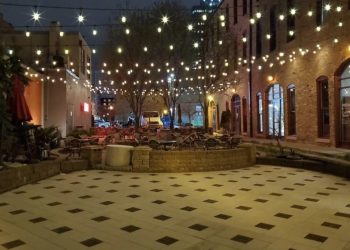 View of Monte Carlo Courtyard landscaping with pavers, a retaining wall and hanging outdoor lights